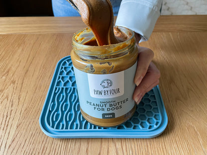 Person pouring peanut butter into a jar labeled 'Paw by Four' on a wooden table.