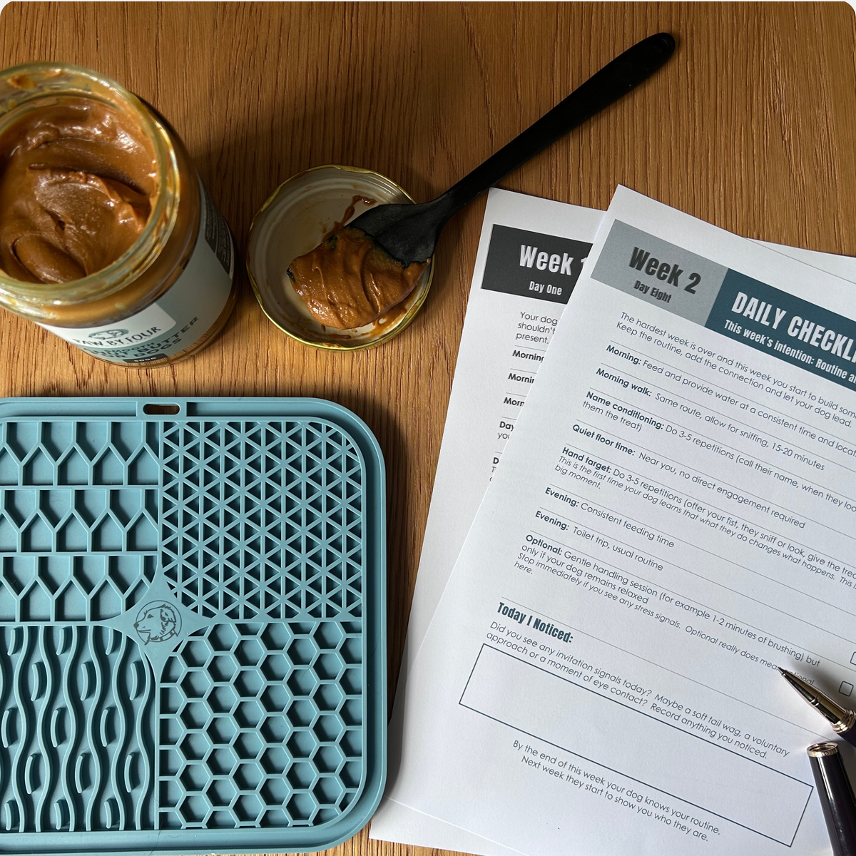 Jar of Paw by Four peanut butter, a blue silicone lick mat, and a daily checklist on a wooden surface.